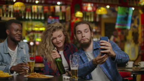 Happy-male-friends-taking-selfie-and-drinking-beer-at-bar-or-pub.-People-leisure-friendship-technology-and-party-concept---happy-male-friends-taking-selfie